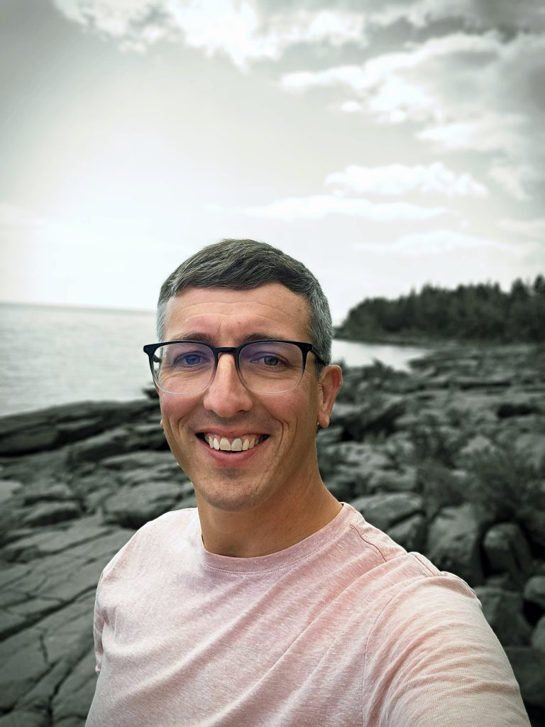 A headshot of Aaron next to Lake Superior. He is in color and the rest is black and white.